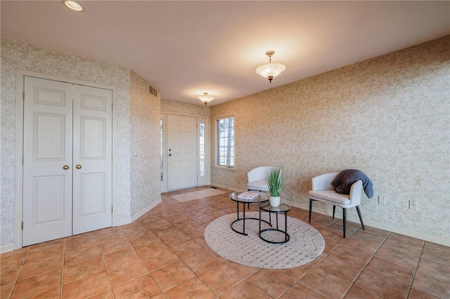 living area with light tile patterned floors, visible vents, wallpapered walls, and baseboards