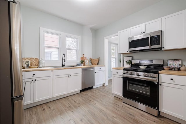 kitchen with light wood-style flooring, a sink, appliances with stainless steel finishes, white cabinets, and wooden counters