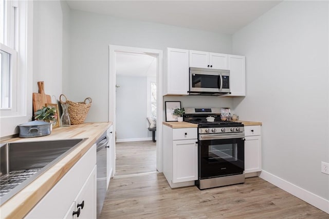 kitchen with light wood-type flooring, appliances with stainless steel finishes, white cabinets, wood counters, and a sink