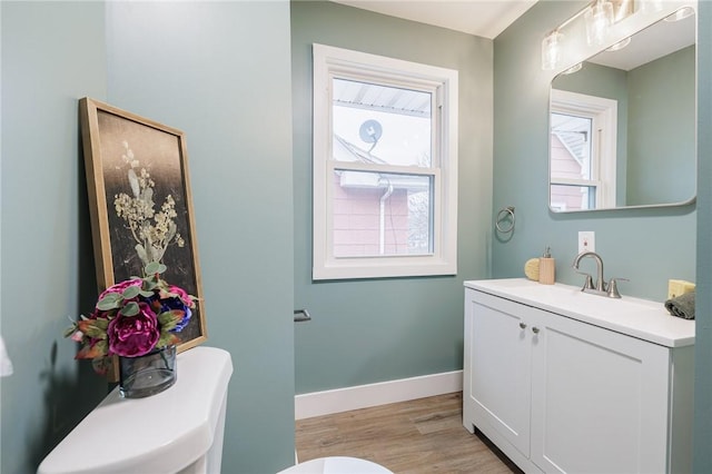 half bath with toilet, wood finished floors, baseboards, and a wealth of natural light