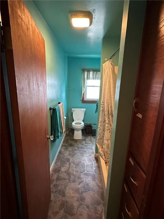 bathroom with curtained shower, toilet, stone finish flooring, and baseboards