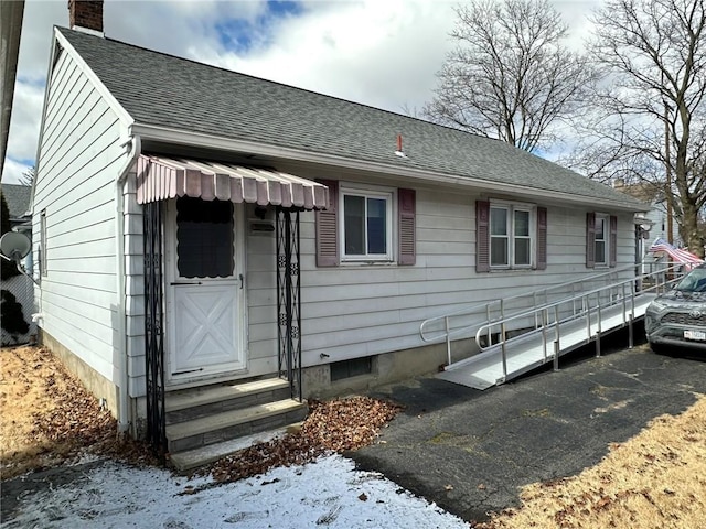 view of front of property with driveway, entry steps, a chimney, and a shingled roof