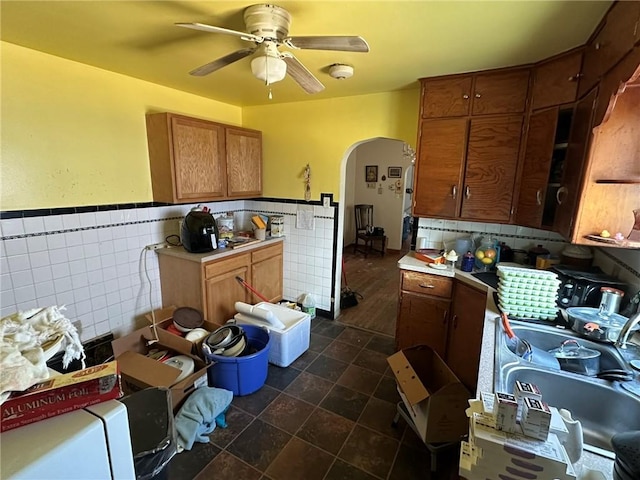 kitchen featuring tile walls, a ceiling fan, arched walkways, and brown cabinets