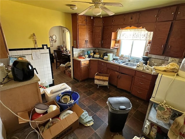 kitchen featuring ceiling fan, a wainscoted wall, arched walkways, tile walls, and a sink