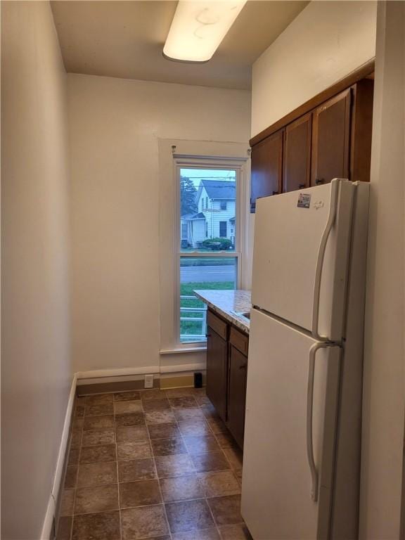 kitchen with light countertops, stone finish floor, baseboards, and freestanding refrigerator