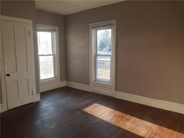 spare room with baseboards and dark wood-type flooring