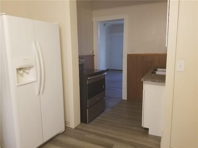 kitchen with dark countertops, white refrigerator with ice dispenser, wood finished floors, stainless steel electric range, and wainscoting