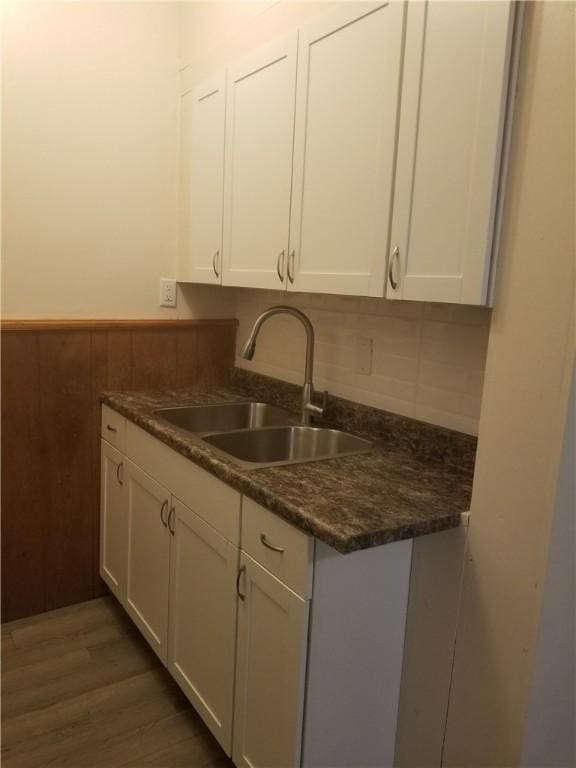 kitchen with a sink, dark countertops, wood finished floors, white cabinets, and wainscoting