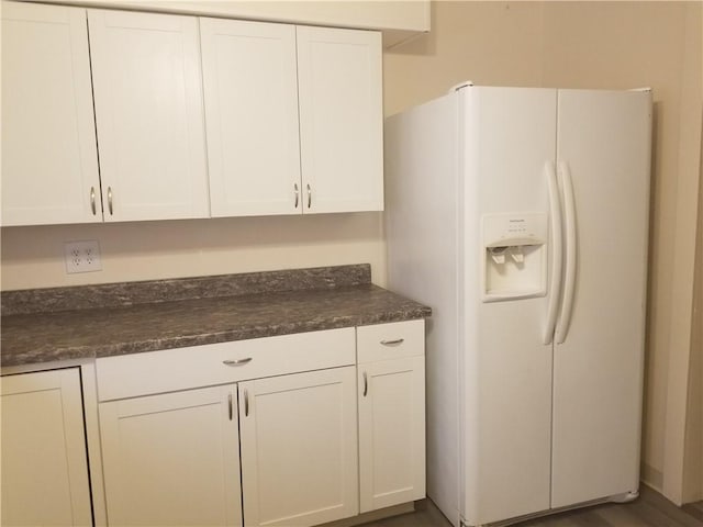 kitchen featuring white fridge with ice dispenser, dark countertops, and white cabinetry