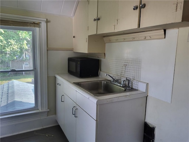 kitchen with a sink, tasteful backsplash, white cabinetry, black microwave, and light countertops