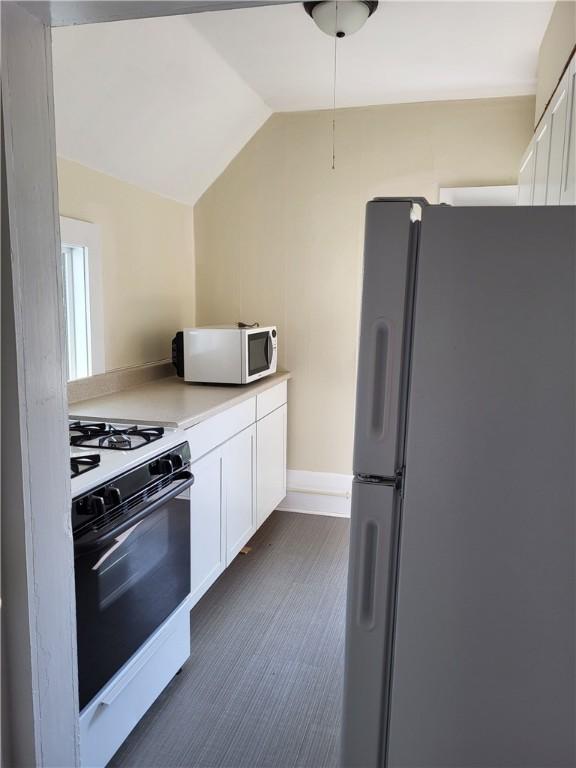 kitchen with white appliances, white cabinets, light countertops, and lofted ceiling