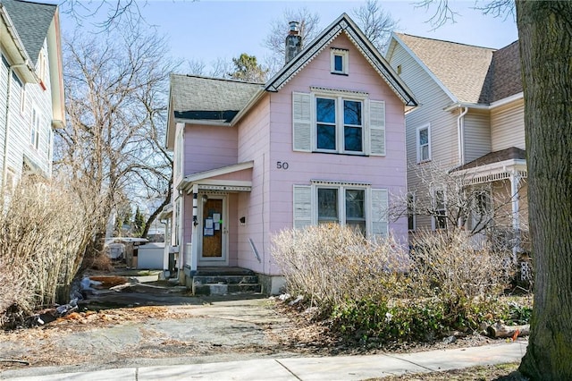 victorian home featuring entry steps, a chimney, and a shingled roof