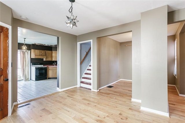 interior space with visible vents, a notable chandelier, light wood-style floors, baseboards, and stairs