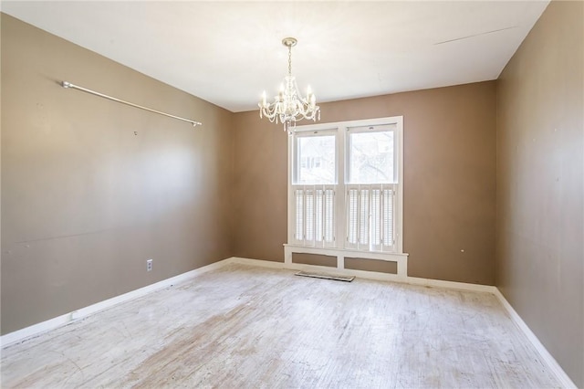 spare room with a notable chandelier, wood finished floors, and baseboards