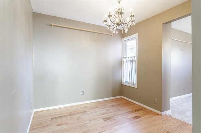 empty room featuring a notable chandelier, light wood-style floors, and baseboards