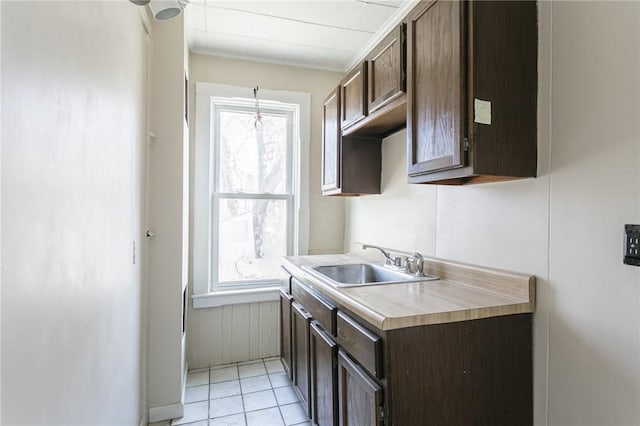 kitchen with a sink, dark brown cabinetry, light tile patterned floors, and light countertops