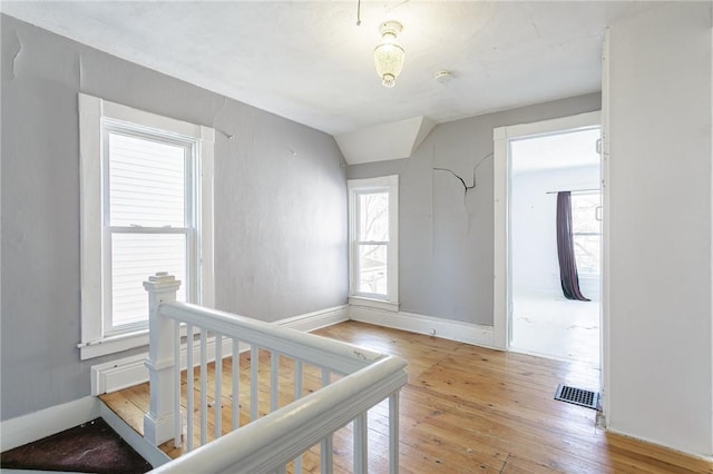 interior space featuring visible vents, baseboards, lofted ceiling, light wood-style floors, and an upstairs landing