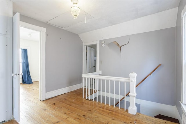 hallway with baseboards, attic access, lofted ceiling, hardwood / wood-style flooring, and an upstairs landing