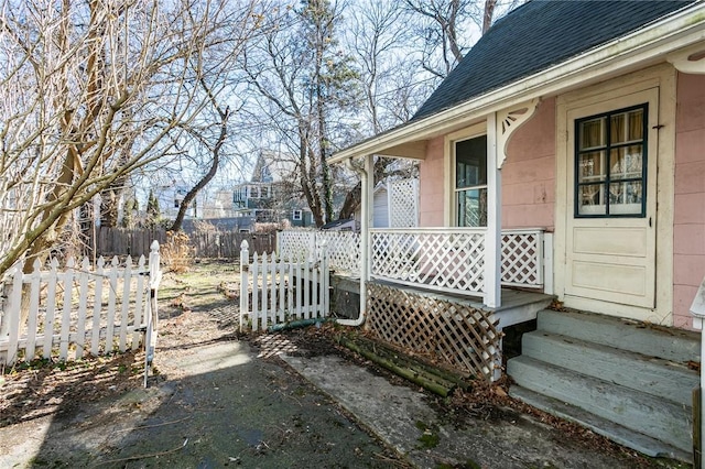 exterior space with fence, covered porch, and roof with shingles