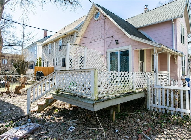 exterior space with a deck, fence, and a shingled roof