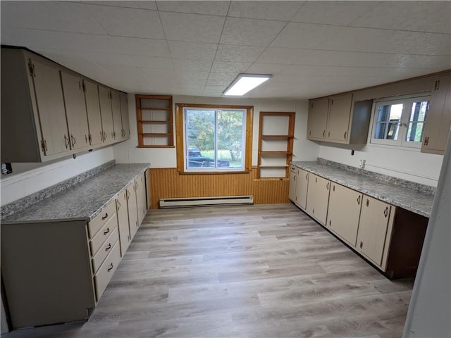 kitchen with light wood finished floors, wooden walls, a baseboard heating unit, light countertops, and wainscoting