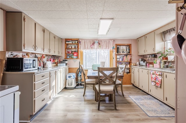 kitchen with stainless steel microwave, cream cabinetry, light countertops, and light wood finished floors