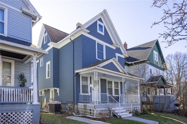 view of front of home with central air condition unit, roof with shingles, a porch, and a chimney