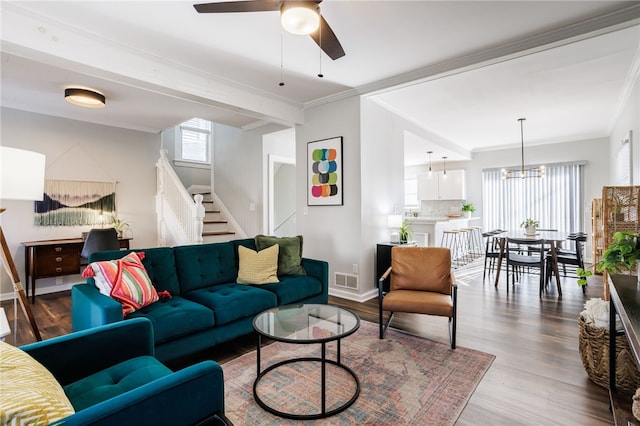 living room featuring baseboards, stairs, ornamental molding, ceiling fan with notable chandelier, and wood finished floors