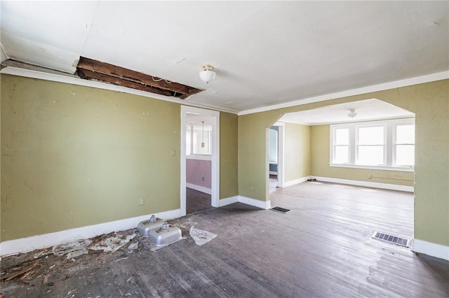 unfurnished room with visible vents, arched walkways, baseboards, and wood finished floors