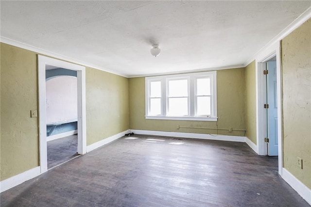 unfurnished room with arched walkways, ornamental molding, baseboards, and wood finished floors