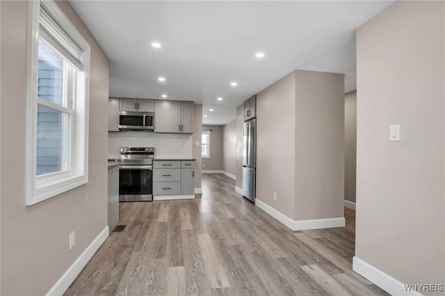 kitchen featuring tasteful backsplash, light countertops, light wood-type flooring, gray cabinets, and appliances with stainless steel finishes