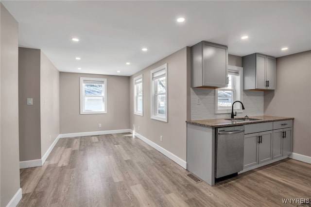 kitchen featuring light wood finished floors, backsplash, gray cabinetry, dishwasher, and a sink