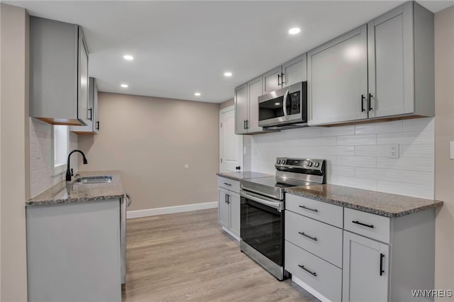 kitchen with a sink, gray cabinetry, stainless steel appliances, light wood-style floors, and tasteful backsplash