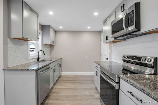 kitchen with dark stone countertops, baseboards, a sink, gray cabinetry, and stainless steel appliances