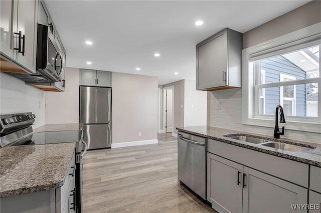 kitchen with dark stone countertops, gray cabinets, appliances with stainless steel finishes, and a sink