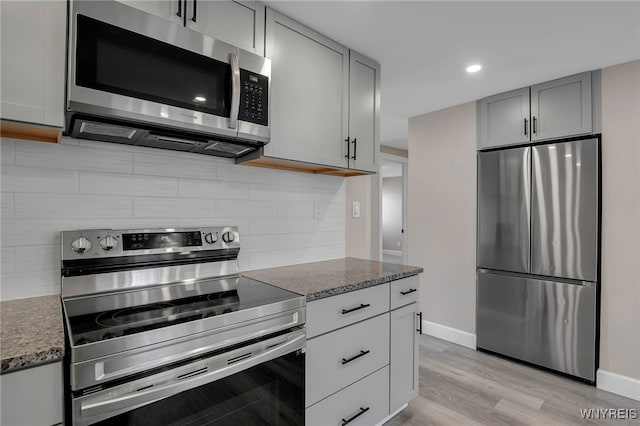 kitchen featuring light stone counters, light wood finished floors, gray cabinetry, appliances with stainless steel finishes, and backsplash