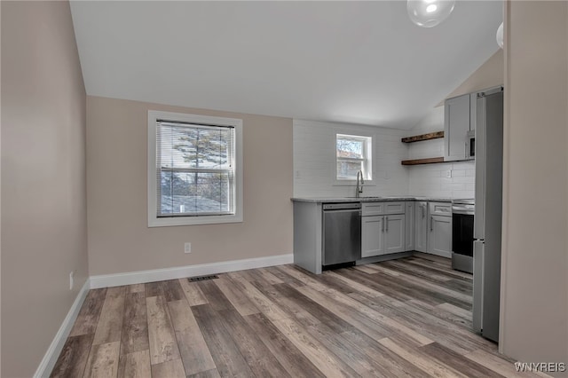 kitchen featuring open shelves, a sink, vaulted ceiling, appliances with stainless steel finishes, and backsplash