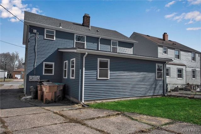 back of property with a chimney, a yard, and fence