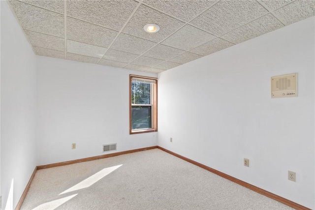 empty room with a paneled ceiling, carpet, visible vents, and baseboards