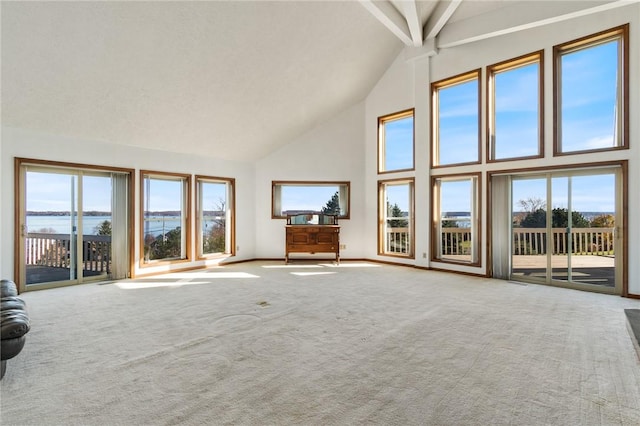 unfurnished living room featuring baseboards, a water view, beamed ceiling, carpet floors, and high vaulted ceiling