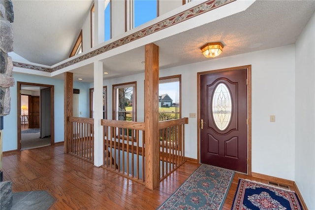 entrance foyer with visible vents, baseboards, wood finished floors, a textured ceiling, and high vaulted ceiling