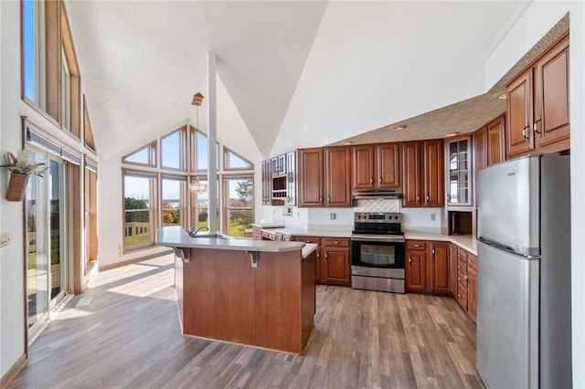 kitchen with a kitchen bar, stainless steel appliances, brown cabinetry, light countertops, and glass insert cabinets