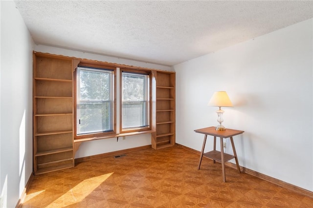 empty room featuring visible vents, a textured ceiling, and baseboards