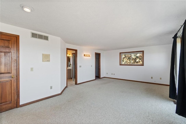 empty room featuring light colored carpet, baseboards, visible vents, and a textured ceiling