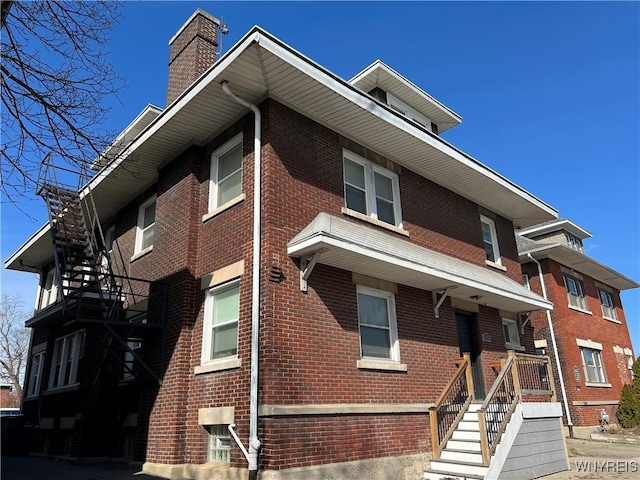 view of front facade featuring brick siding, stairway, and a chimney