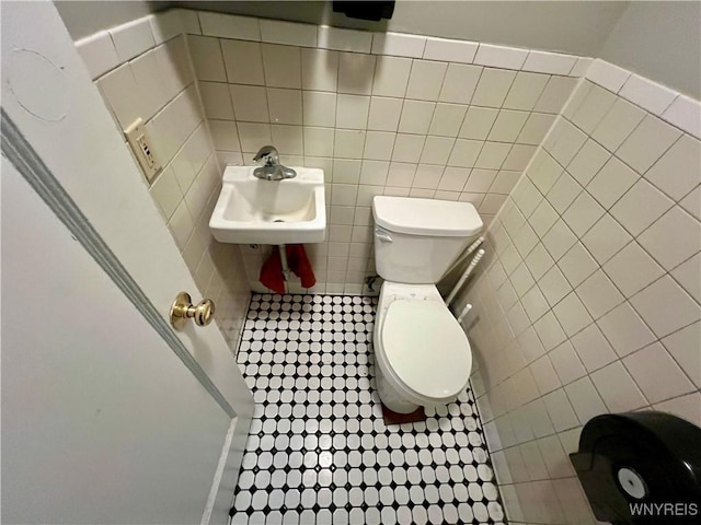 half bath featuring toilet, tile walls, and a sink