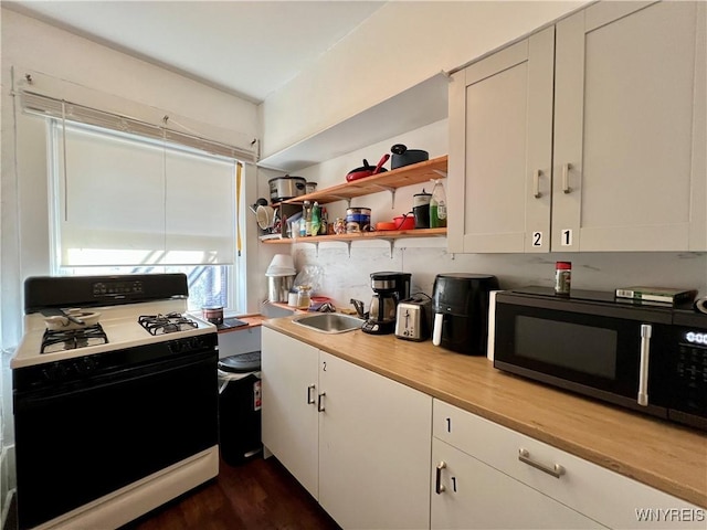 kitchen featuring gas range, white cabinets, black microwave, and a sink