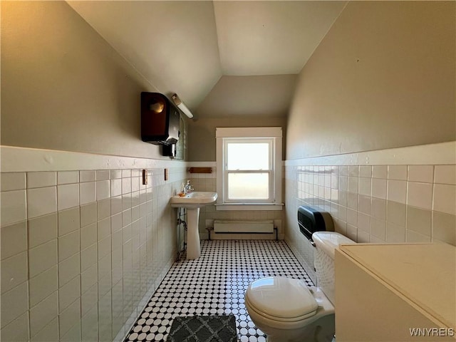 half bathroom featuring toilet, a sink, tile walls, wainscoting, and vaulted ceiling