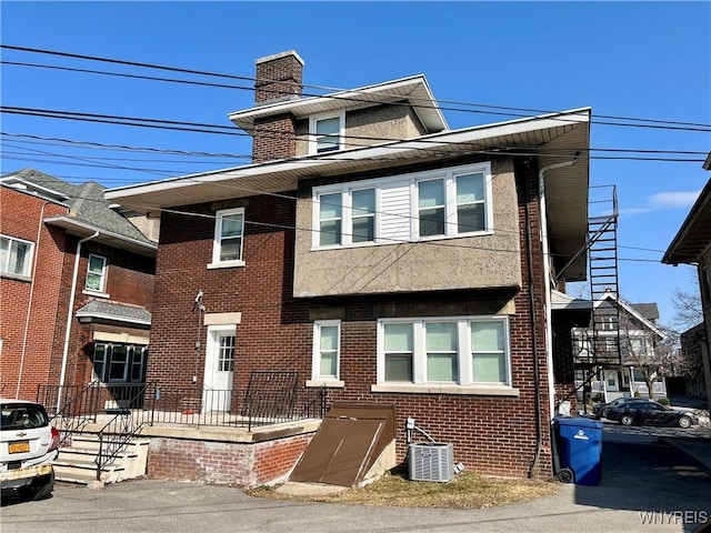 view of front of house with brick siding, a chimney, and central AC