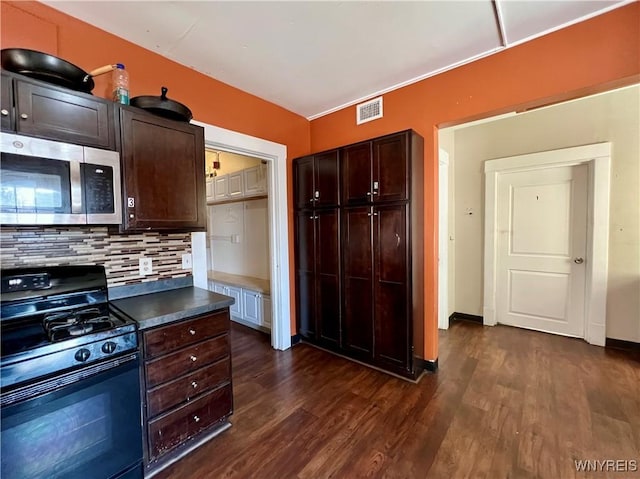 kitchen with dark wood-style floors, visible vents, black gas range, stainless steel microwave, and backsplash